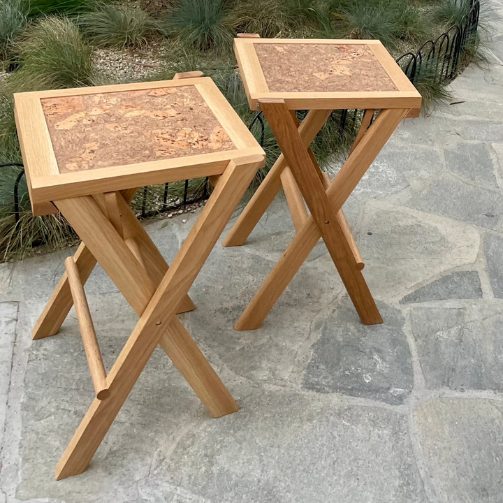 The LAPILO Folding Stool by Earl Home features an angular solid wood frame with a marbled cork seat and cross-legged design in a sleek finish.