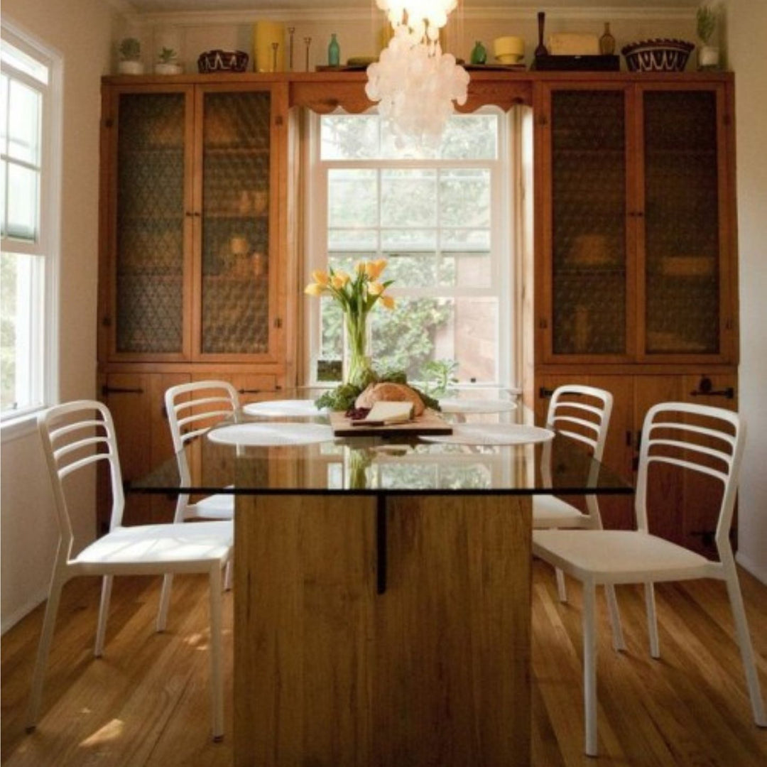 The LUXE Dining Table by Earl Home features a polished glass top and a wooden base with natural wood grain and geometric lines. Solid maple uprights with a walnut spine.