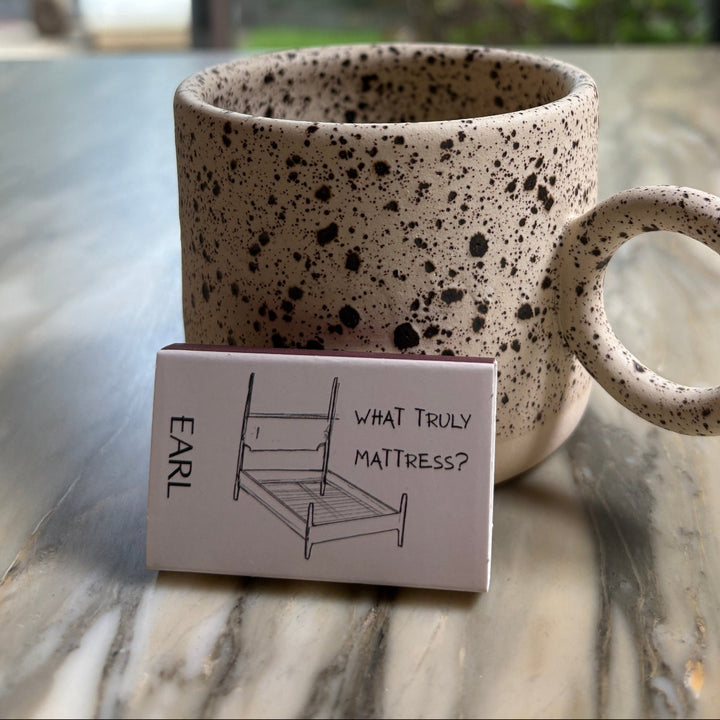 Speckled ceramic mug with a handle on a marble surface, with a blurred outdoor background