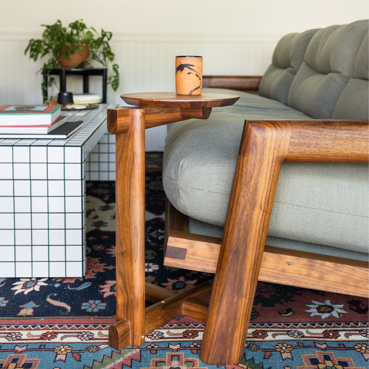 The Walnut MEDIA Side Table by Earl Home is a beautifully crafted nesting table featuring a solid wood construction with a round top and a custom-designed T-shaped base.