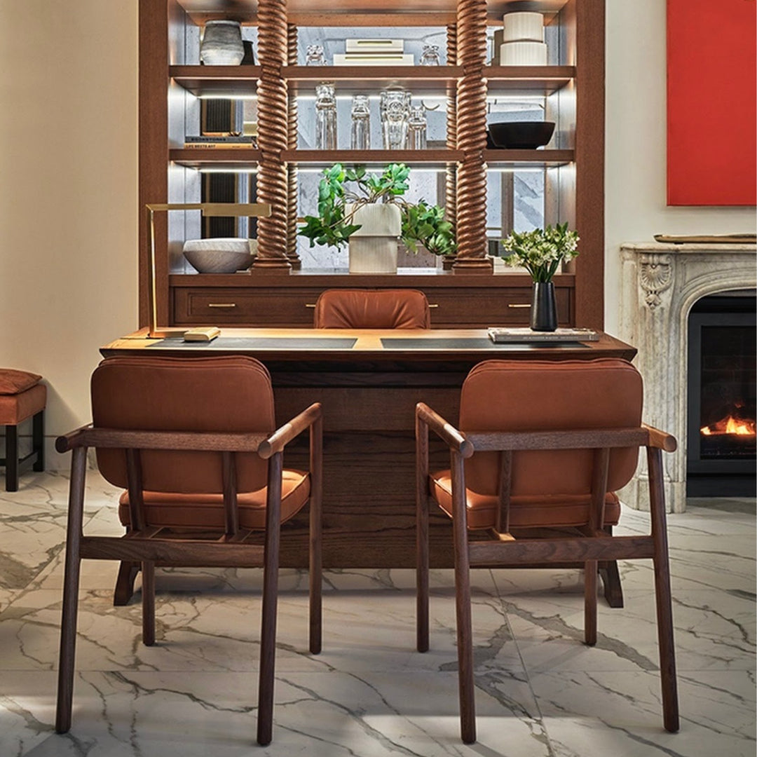 The MORESBY Captain Chair by Earl Home is hand-made with a custom upholstered camel leather seat that is a rich brown leather and walnut solid wood, set against a white background. Here shown at The Pendry Hotel Concierge desk.