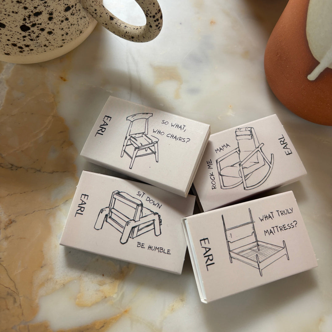 Small matchboxes labeled 'EARL' with illustrations on a marble surface with ceramic items.