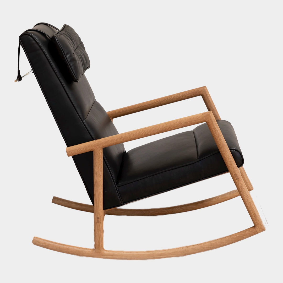 Side view of the MORESBY Rocker by Earl Home. This handmade wooden rocking chair features solid wood construction, black leather cushions, a custom upholstered seat, and an attached headrest.