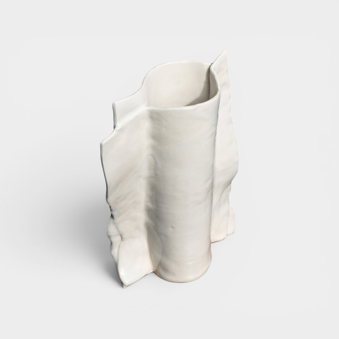 White ceramic vase art form with wavy design on a light gray background Beige or ivory ceramic vase in high gloss with dried plants and flowers on a wooden vintage chair against a gray lime wash wall with an ornate floral mirror.