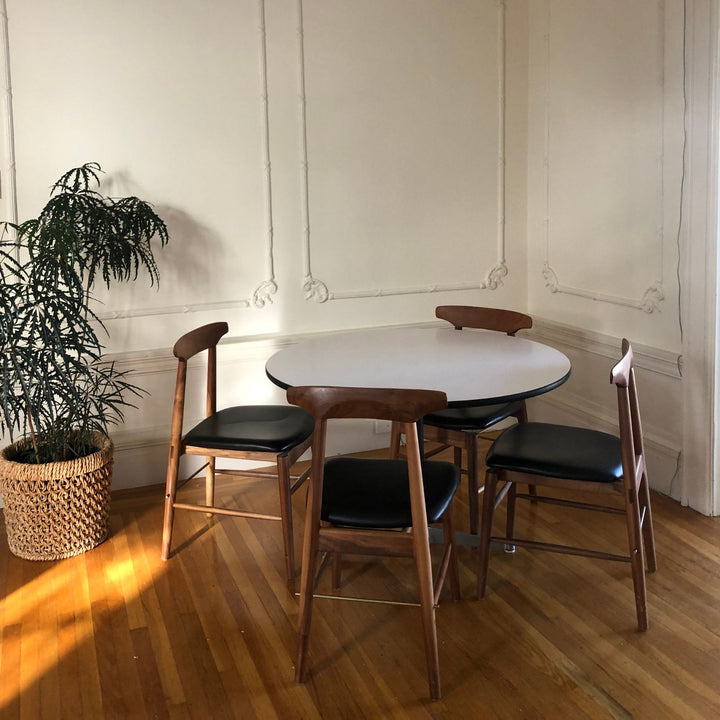 The Earl Home SABLE Dining Chair features a hand-made, bespoke charcoal fumed walnut wooden design with a curved backrest and four legs. Its flat seat exemplifies minimalist elegance, crafted from solid wood for lasting durability. Black leather upholstery.