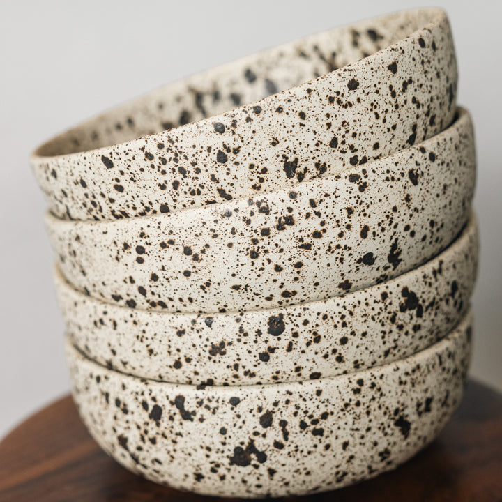 Stack of speckled ceramic bowls on a wooden surface with a neutral background