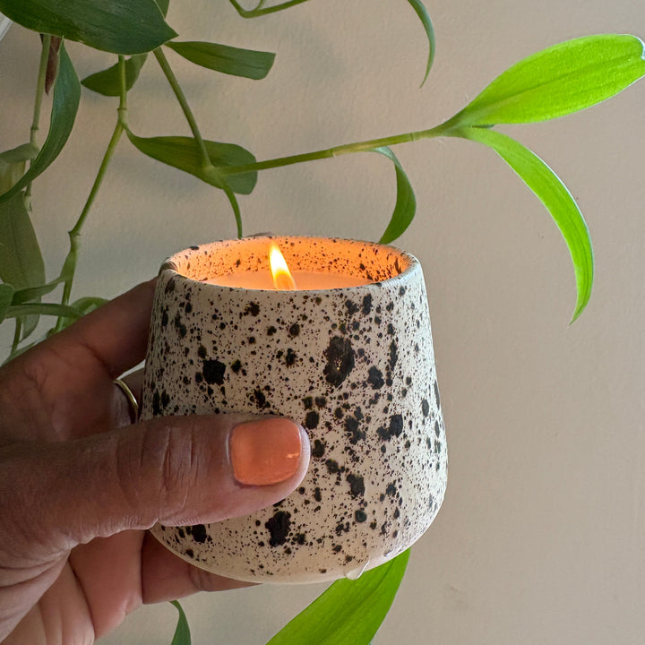 Speckled ceramic candle held by a hand with a plant in the background. Handmade in los Angeles, California. Made in America.