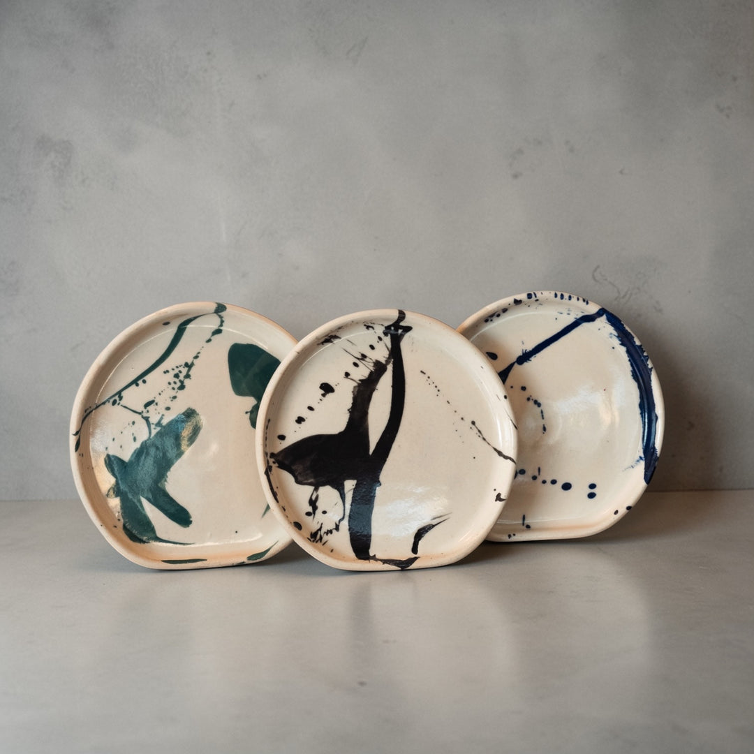 Three ceramic plates with abstract designs on a gray background