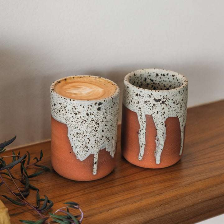 Two ceramic cups with speckled glaze on a wooden surface.