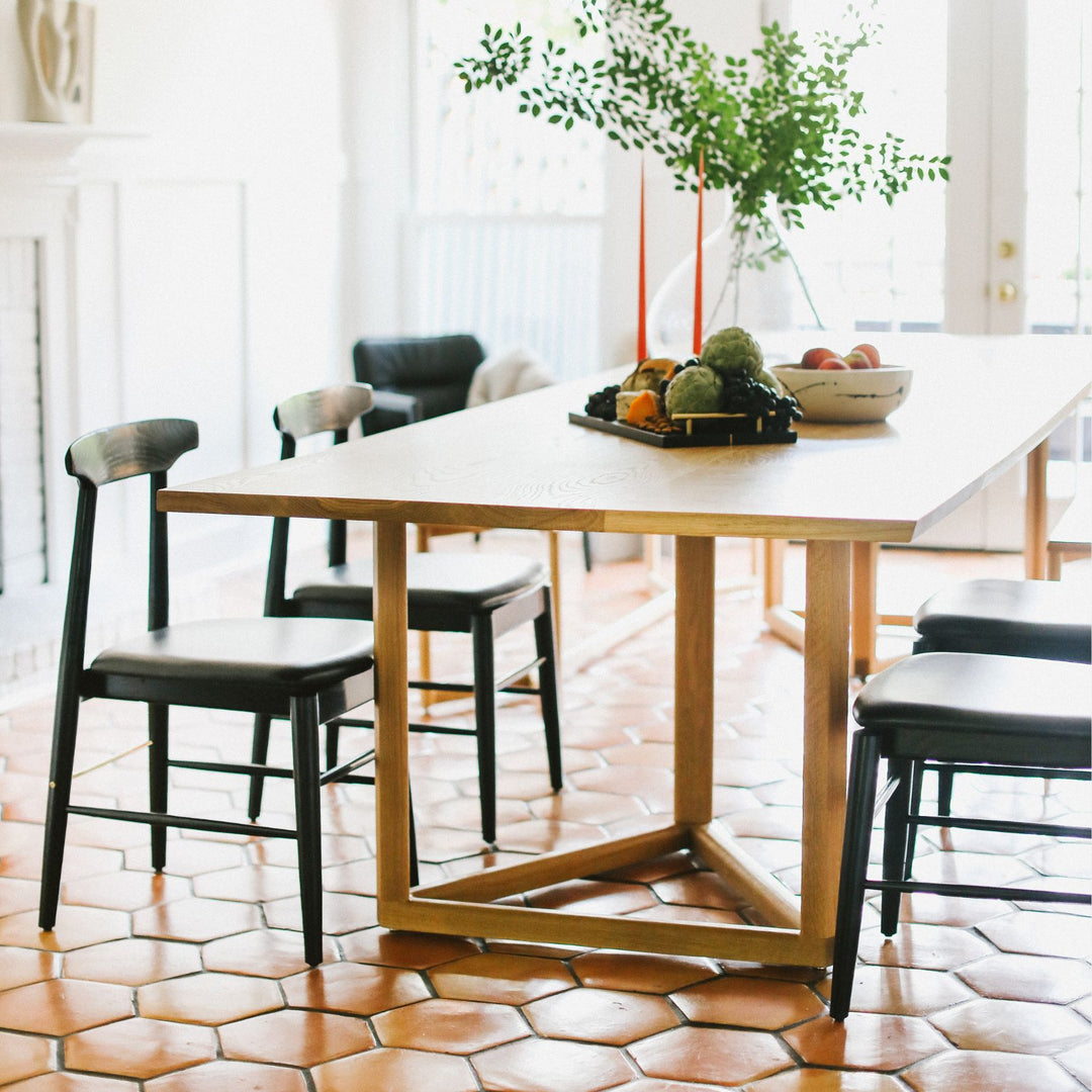 The WOLF Dining Table by Earl Home features a long, oval solid wood design with two geometric triangular legs, elegantly displayed to highlight the beauty of unique wood furniture. available in walnut, white oak, or ebonized oak, with a pill, rectangular or live edge table top.