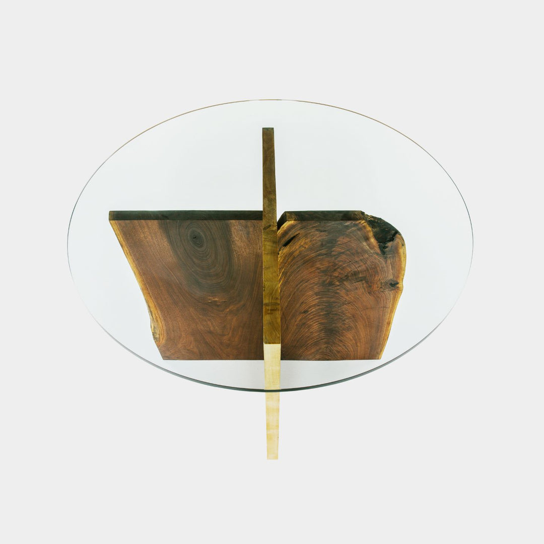 The X Dining Table by Earl Home is a handcrafted, round glass table with intersecting walnut and maple slabs, showcasing its natural organic edge and epitomizing wood slab artistry.