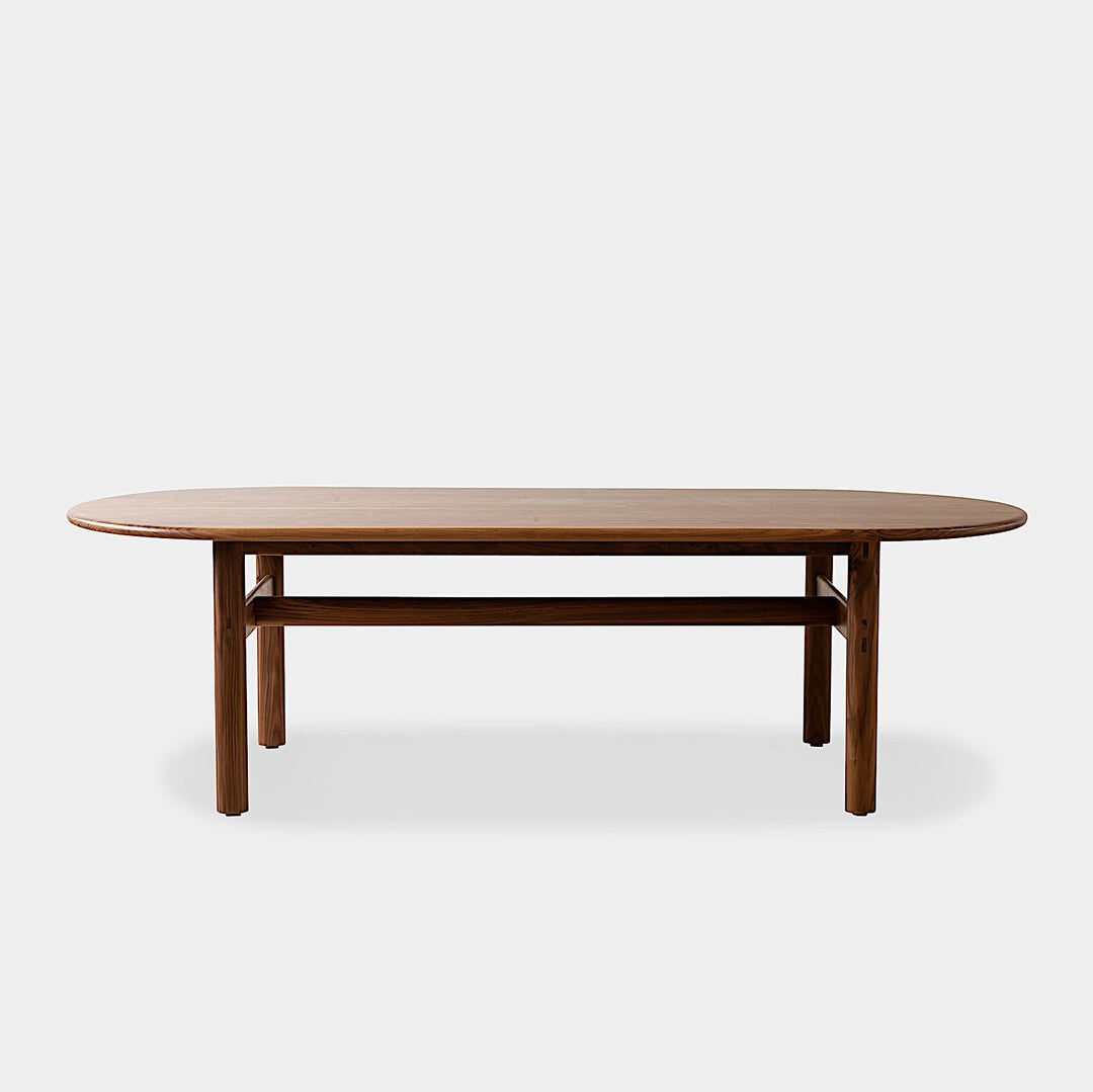 The PALANG Dining Table by Earl Home boasts a robust oval design in rich walnut, supported by four legs and a crossbeam. It comes on a plain white background and offers customizable lengths for perfect fitting in any space.