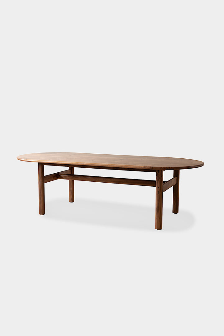 The PALANG Dining Table by Earl Home boasts a robust oval design in rich walnut, supported by four legs and a crossbeam. It comes on a plain white background and offers customizable lengths for perfect fitting in any space.