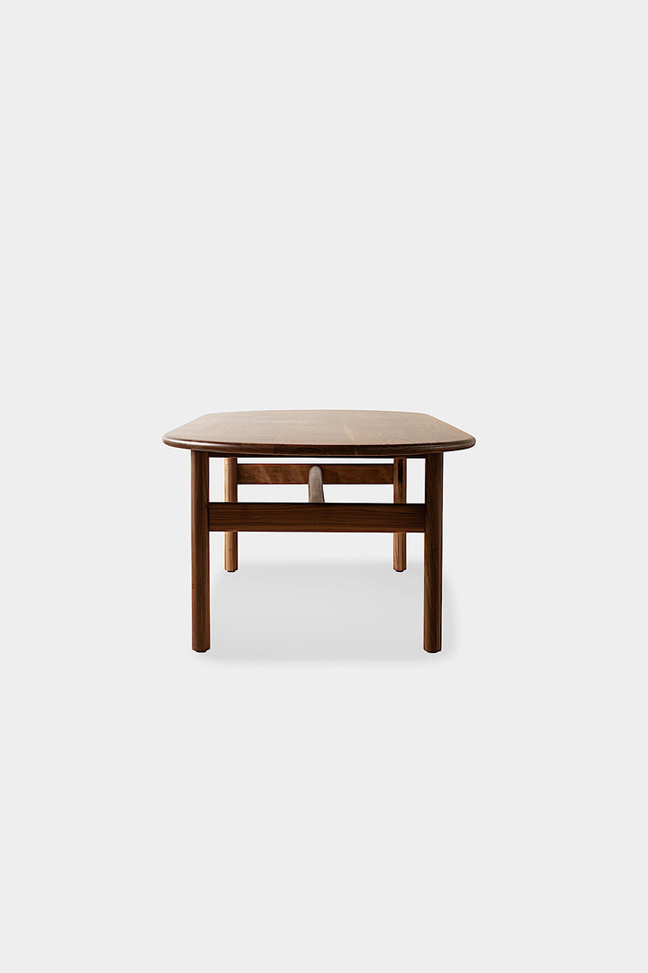 The PALANG Dining Table by Earl Home boasts a robust oval design in rich walnut, supported by four legs and a crossbeam. It comes on a plain white background and offers customizable lengths for perfect fitting in any space.