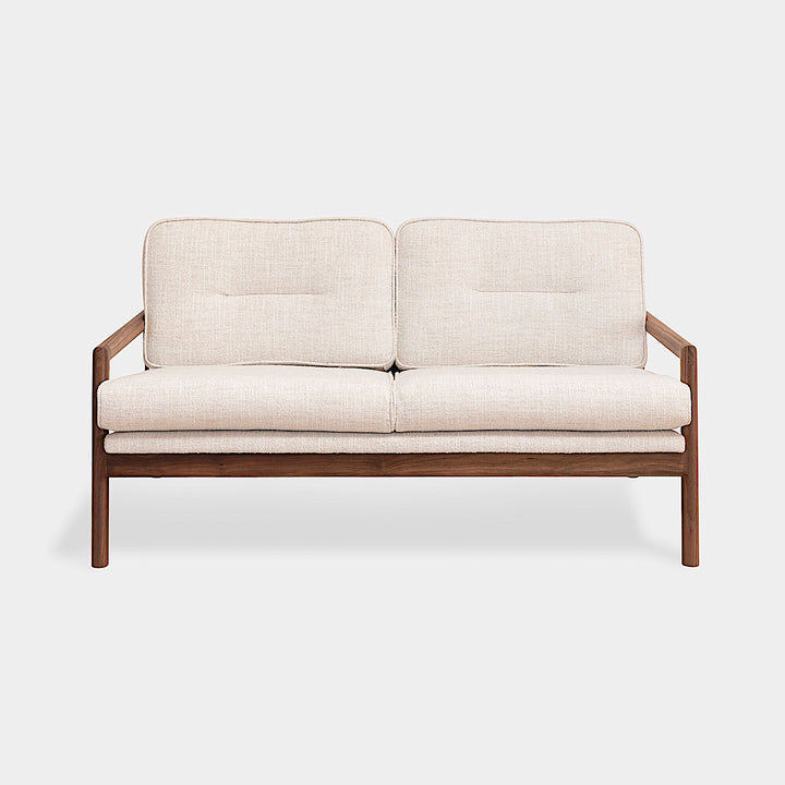 A side view of the MORESBY Love Seat by Earl Home, showcasing solid wood construction and off-white custom upholstered cushions against a plain background.