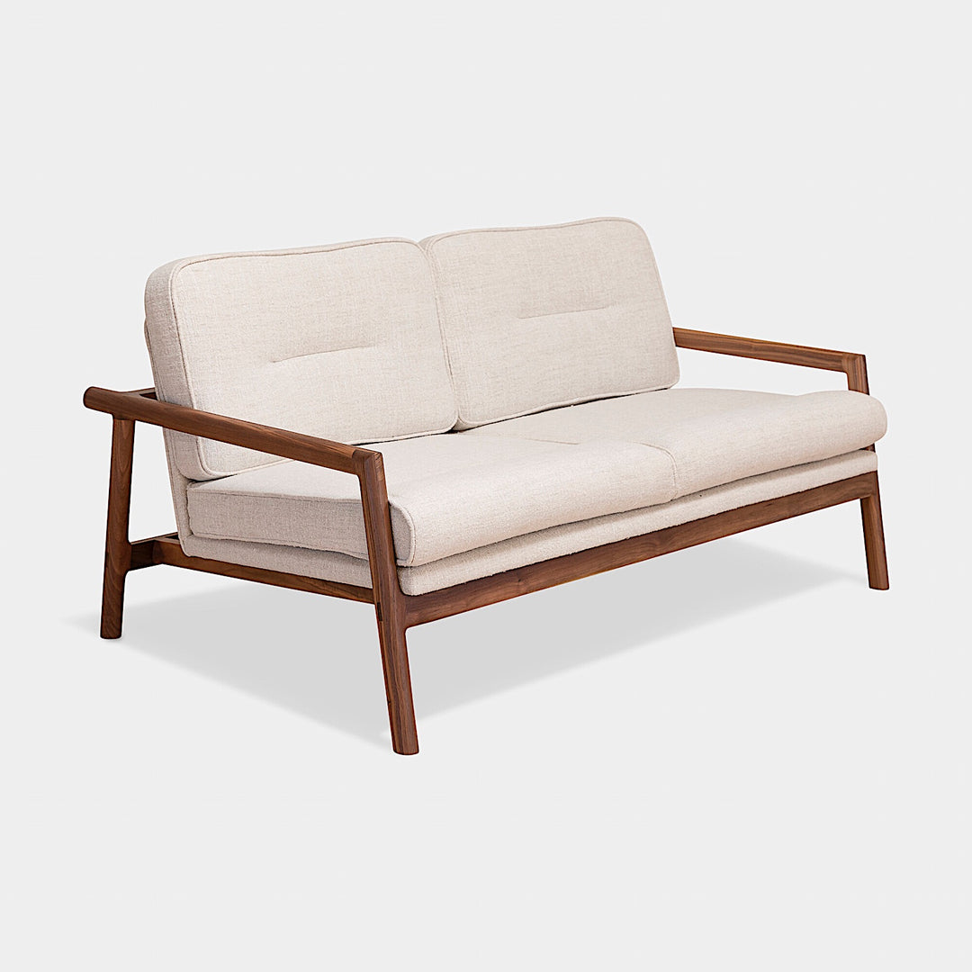 A side view of the MORESBY Love Seat by Earl Home, showcasing solid wood construction and off-white custom upholstered cushions against a plain background.