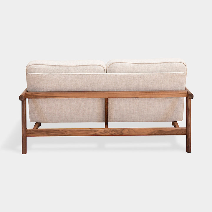 A side view of the MORESBY Love Seat by Earl Home, showcasing solid wood construction and off-white custom upholstered cushions against a plain background.