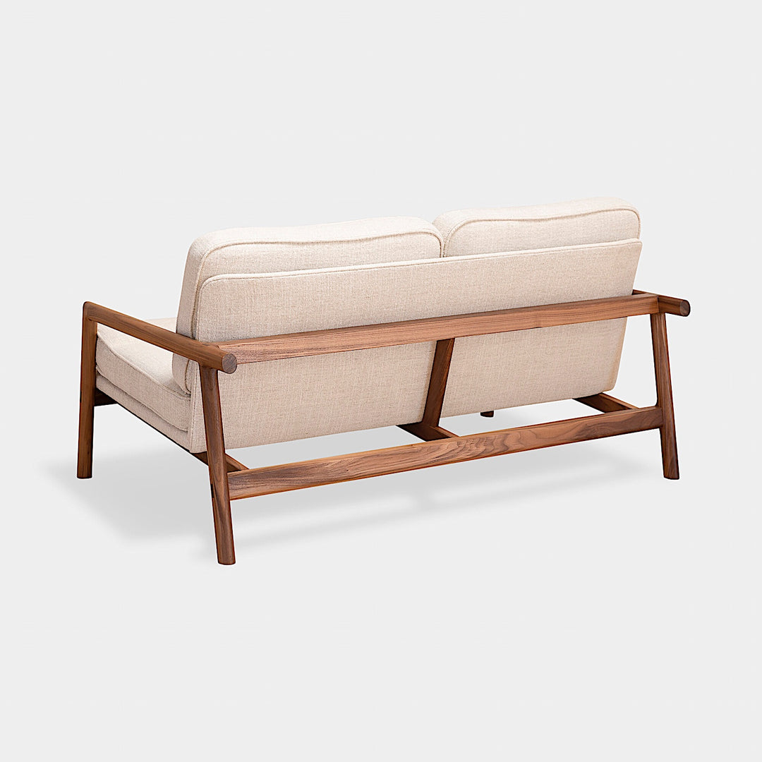 A side view of the MORESBY Love Seat by Earl Home, showcasing solid wood construction and off-white custom upholstered cushions against a plain background.