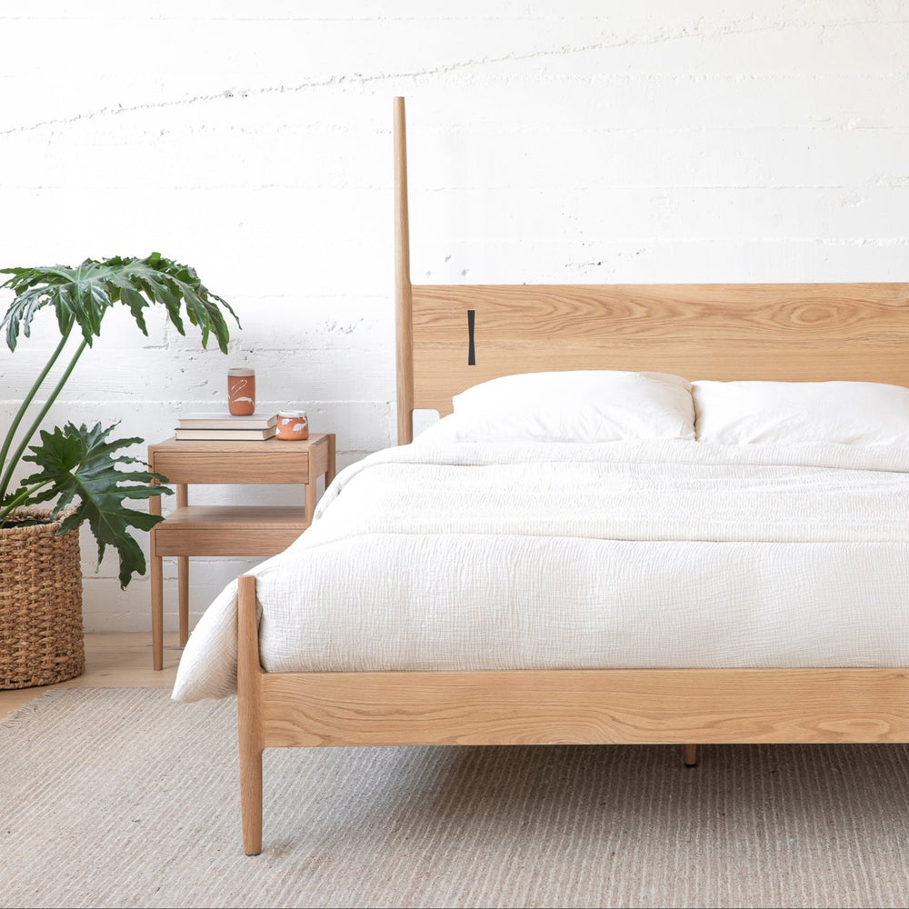 The DANSK Bed by Earl Home features a solid white oak wood frame with a tall headboard and luxurious white bedding, creating your perfect sanctuary. Crafted in walnut, it exemplifies quality and is handmade to order.