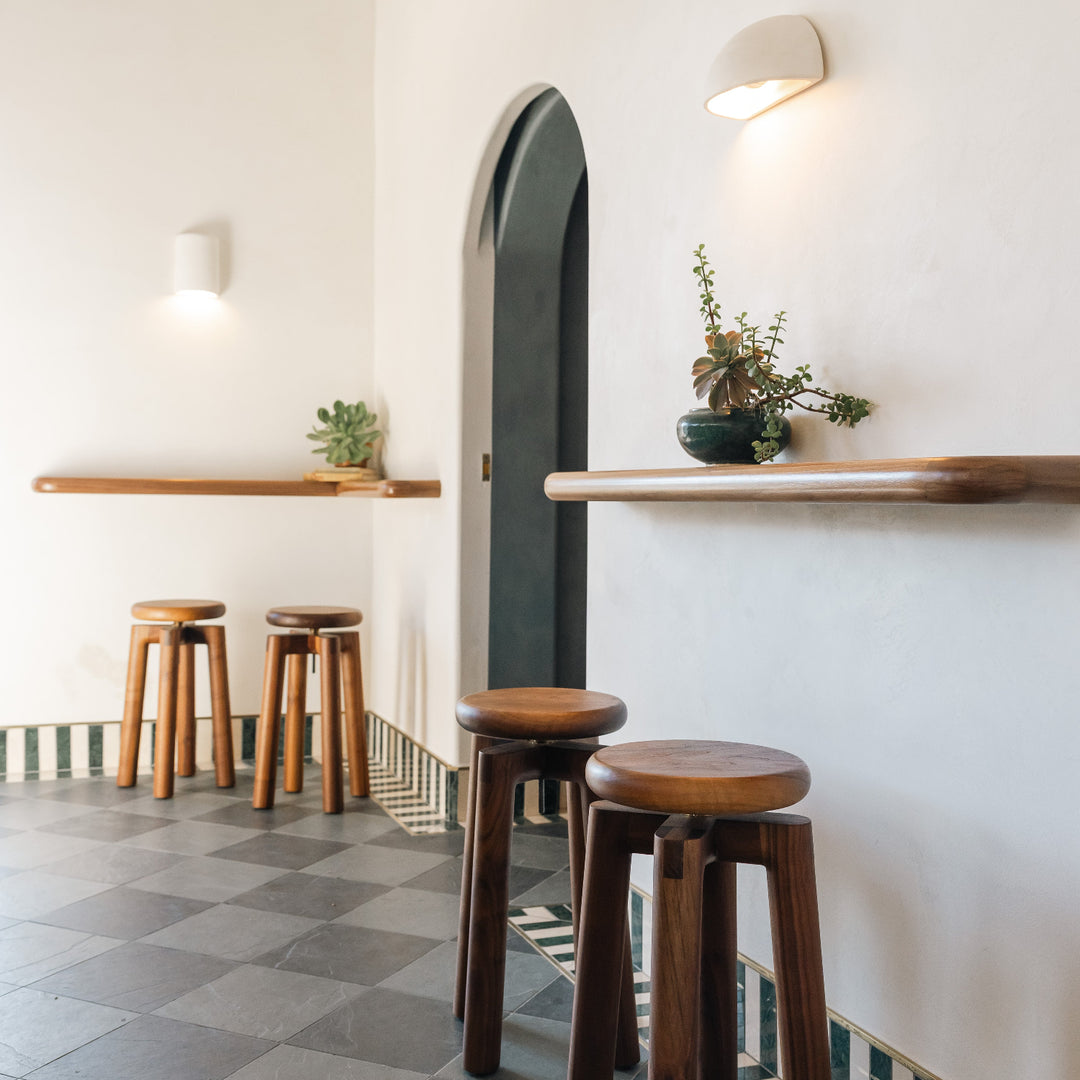 Wooden walnut stools in a modern interior setting with white walls and a checkered floor. 