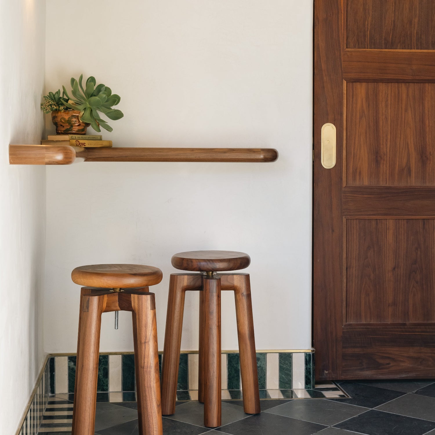 Two wooden stools in a room with a white wall, wooden door, and tiled floor.