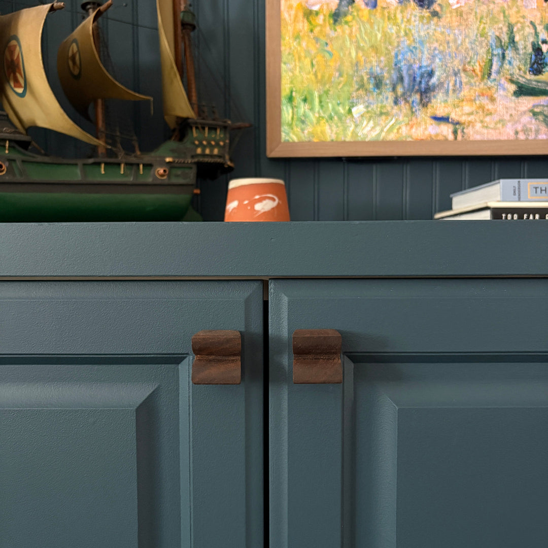 Teal cabinet with decorative items including a painting and a ceramic candle with custom wood cabinet knobs