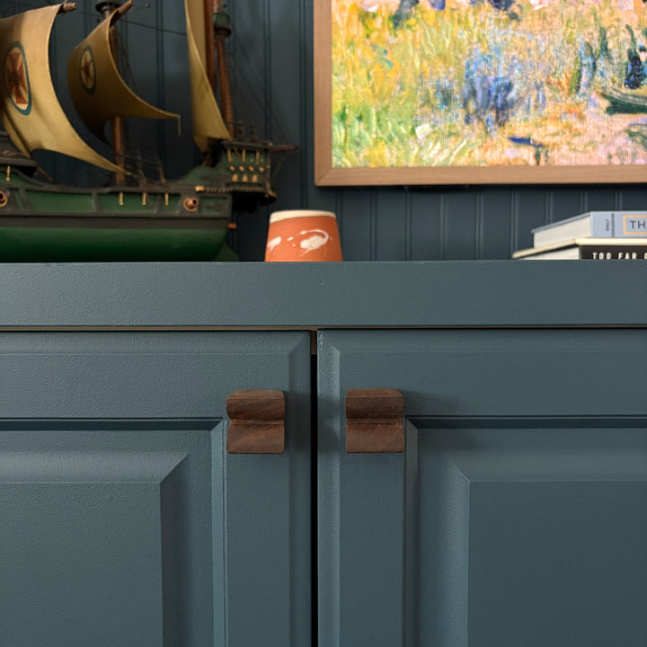 Teal cabinet with decorative items including a painting and a ceramic candle with custom wood cabinet knobs