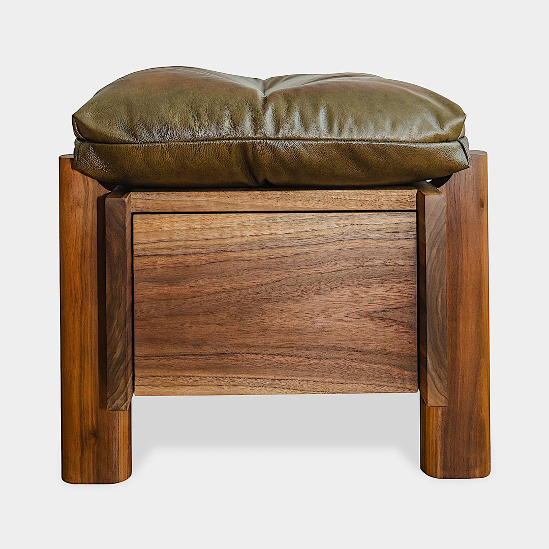 The TAMBU Ottoman by Earl Home is a stylish, handmade piece featuring a green cushioned top and offers storage seating against a white background.