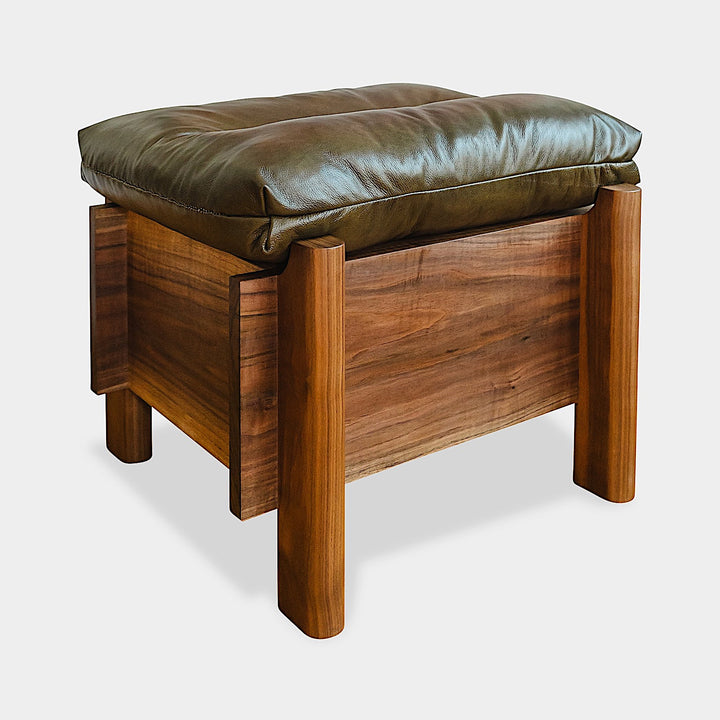 The TAMBU Ottoman by Earl Home is a stylish, handmade piece featuring a green cushioned top and offers storage seating against a white background.