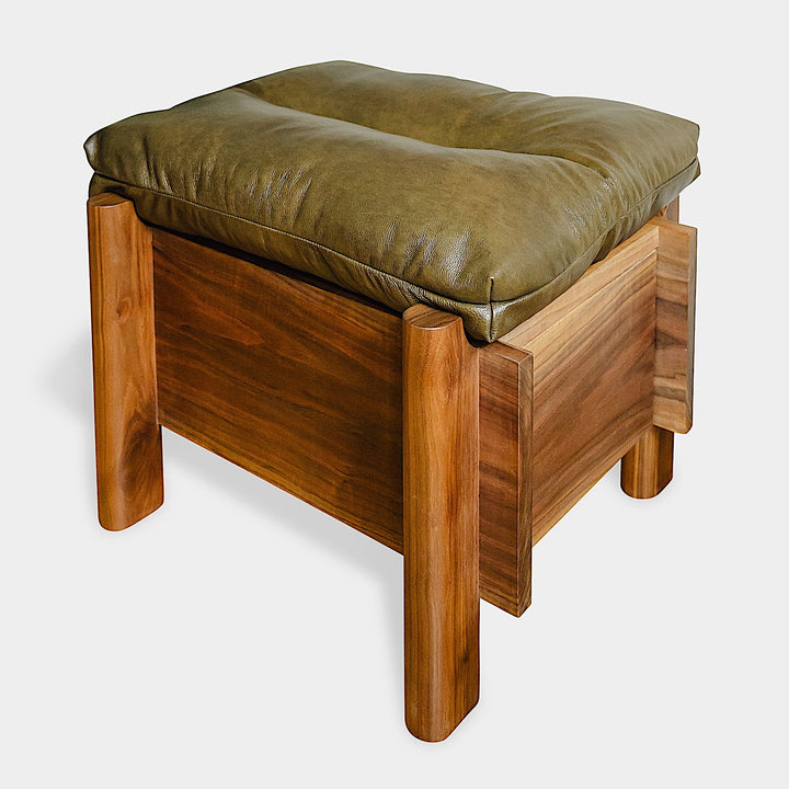 The TAMBU Ottoman by Earl Home is a stylish, handmade piece featuring a green cushioned top and offers storage seating against a white background.