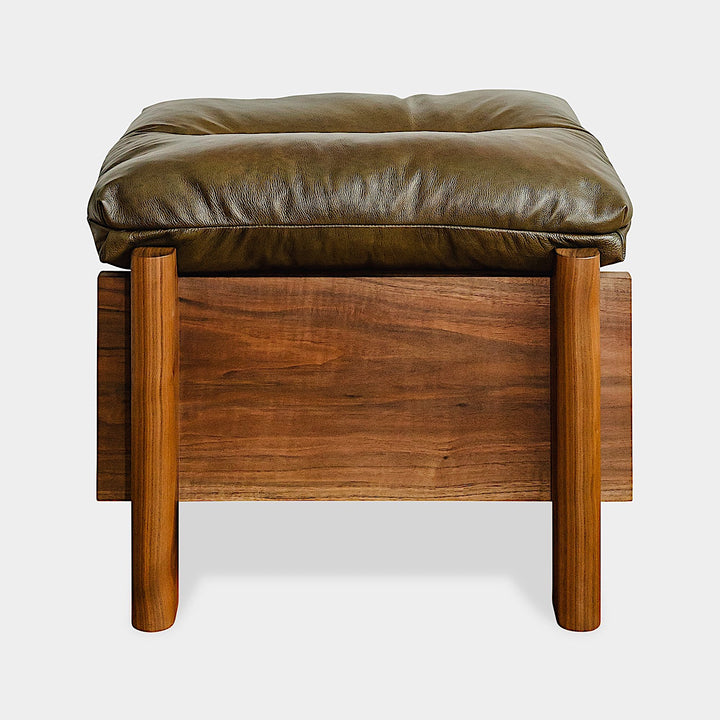 The TAMBU Ottoman by Earl Home is a stylish, handmade piece featuring a green cushioned top and offers storage seating against a white background.