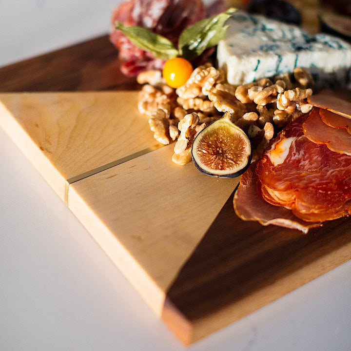 The RECTANGLE Cheese Board by Earl Home is a handcrafted serving board featuring a natural wood grain and accented with an off-center pale triangle on the left, ideal for elegant entertaining.