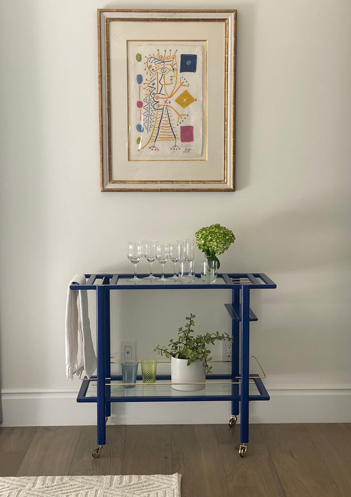 The BAR Cart from Earl Home is a solid wood bar cart on wheels with exquisite hand-cut joinery, featuring two shelves: a robust wood top and an elegant lower shelf made of tempered glass panels.