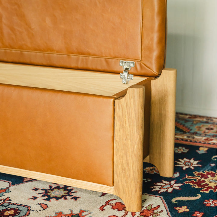 The Earl Home KABOT Storage Trunk is a stylish and practical piece with tan leather upholstery. It features an open lid that reveals a wooden interior with hinged supports, combining elegance and functionality.