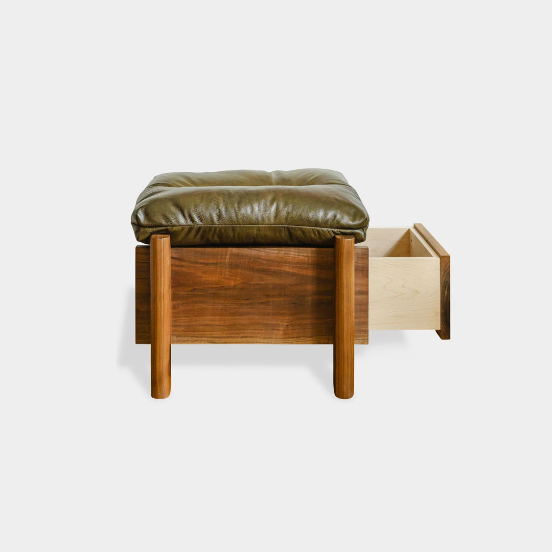 The LAPILO Ottoman by Earl Home is a stylish, handmade piece featuring a green cushioned top and offers storage seating against a white background.