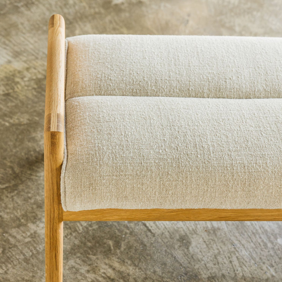 The Earl Home MORESBY Bench highlights a plush light cushion on a solid wood frame, featuring clean lines and a minimalist design. Available in Walnut, Ebonized Oak, or White Oak with a custom upholstered cushion.