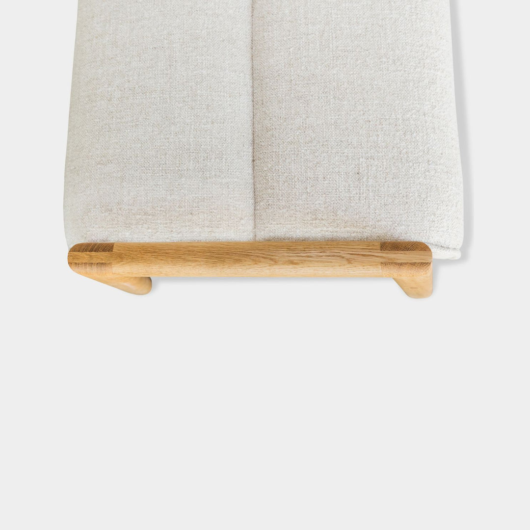 The Earl Home MORESBY Bench highlights a plush light cushion on a solid wood frame, featuring clean lines and a minimalist design. Available in Walnut, Ebonized Oak, or White Oak with a custom upholstered cushion.