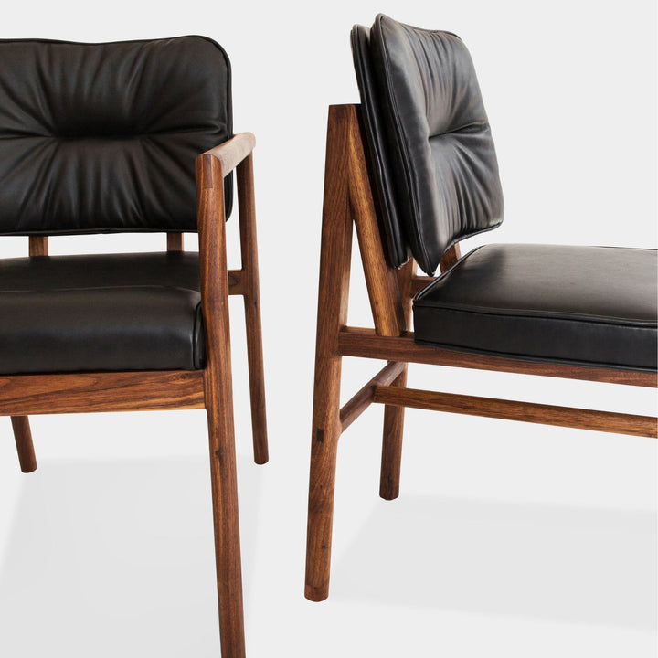 The MORESBY Dining Chair by Earl Home features a custom upholstered black leather seat and backrest, elegantly crafted on a solid wood walnut frame with simple, angular lines.