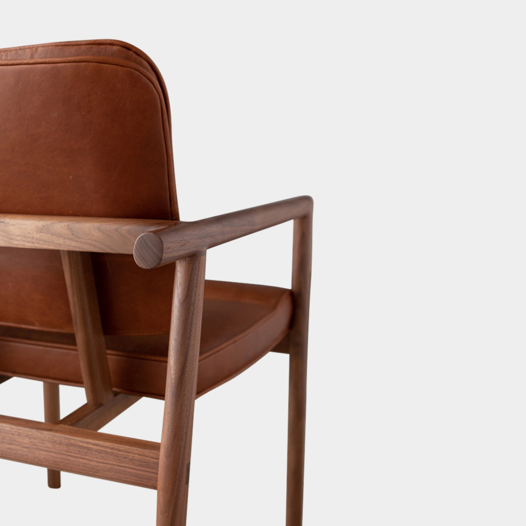 The MORESBY Captain Chair by Earl Home is hand-made with a custom upholstered camel leather seat that is a rich brown leather and walnut solid wood, set against a white background.