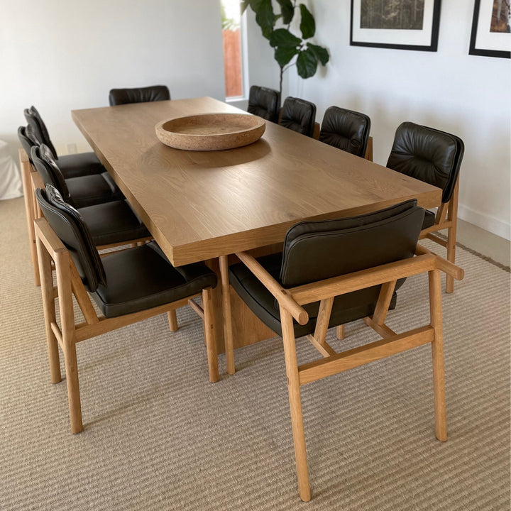 The MORESBY Captain Chair by Earl Home is hand-made with a custom upholstered olive leather seat that is a rich brown leather and white oak solid wood, set in a dining room in the Pacific Palisades, California.