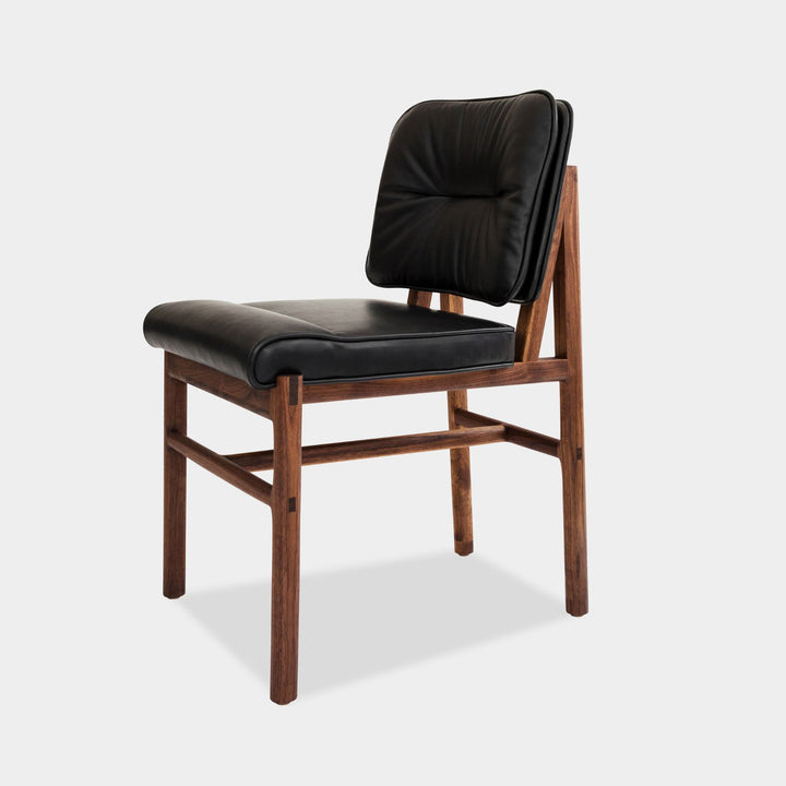 The MORESBY Dining Chair by Earl Home features a custom upholstered black leather seat and backrest, elegantly crafted on a solid wood walnut frame with simple, angular lines.