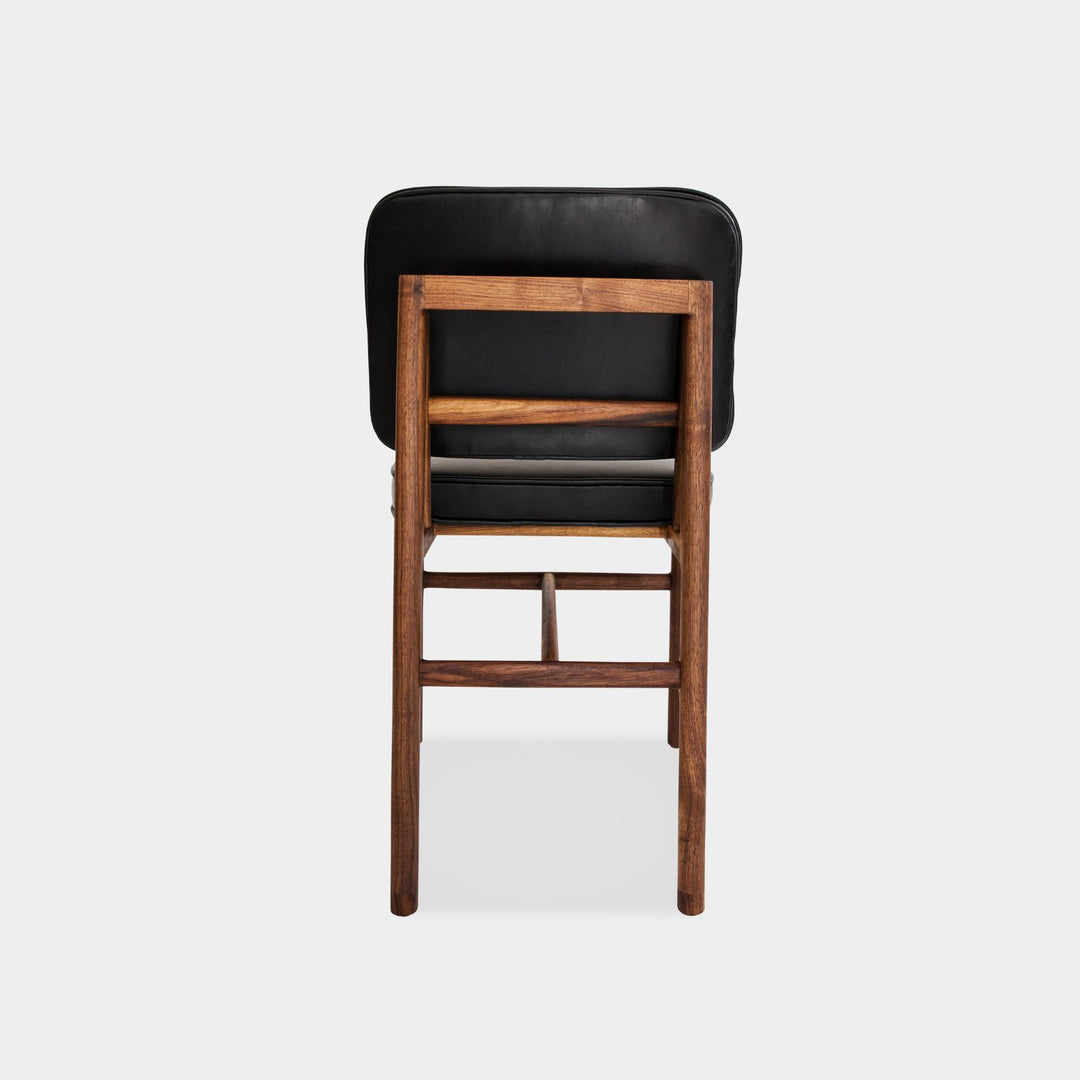 The MORESBY Dining Chair by Earl Home features a custom upholstered black leather seat and backrest, elegantly crafted on a solid wood walnut frame with simple, angular lines.