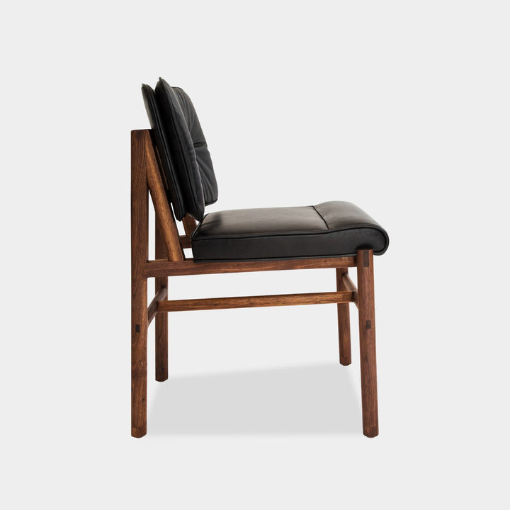 The MORESBY Dining Chair by Earl Home features a custom upholstered black leather seat and backrest, elegantly crafted on a solid wood walnut frame with simple, angular lines.