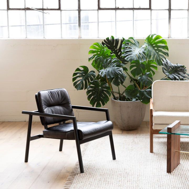 The MORESBY Lounge Chair by Earl Home is a modern, handmade piece featuring a sleek black ebonized oak frame and a custom upholstered black leather cushion.