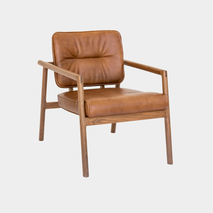 The MORESBY Lounge Chair by Earl Home is a modern, handmade piece featuring a sleek walnut frame and a custom upholstered camel leather cushion.