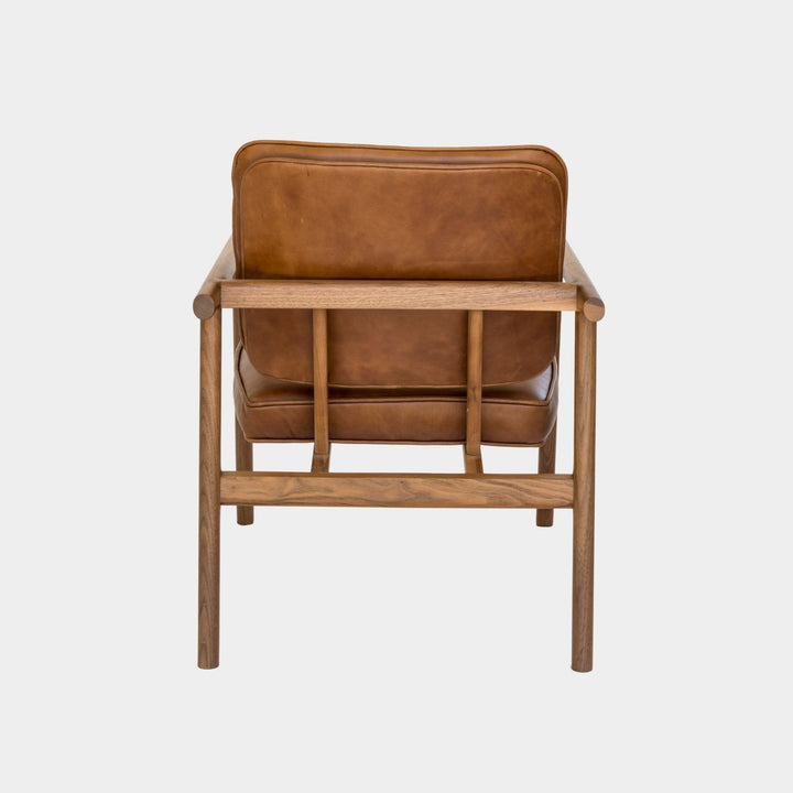 The MORESBY Lounge Chair by Earl Home is a modern, handmade piece featuring a sleek walnut frame and a custom upholstered camel leather cushion.