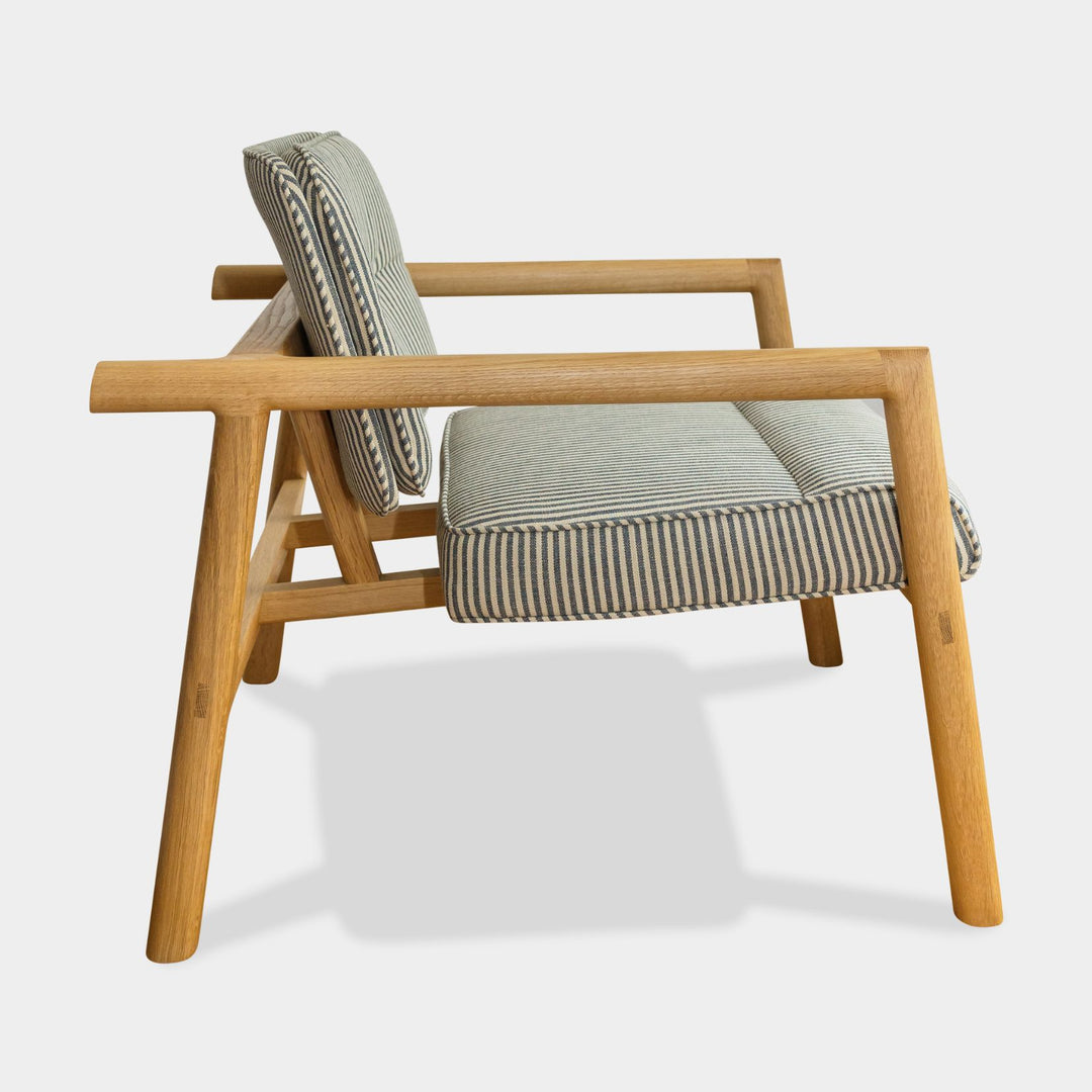 The MORESBY Lounge Chair by Earl Home is a modern, handmade piece featuring a sleek white oak frame and a custom upholstered perennials striped performance fabric cushion.