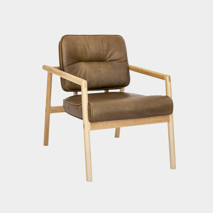 The MORESBY Lounge Chair by Earl Home is a modern, handmade piece featuring a sleek white oak frame and a custom upholstered olive leather cushion.