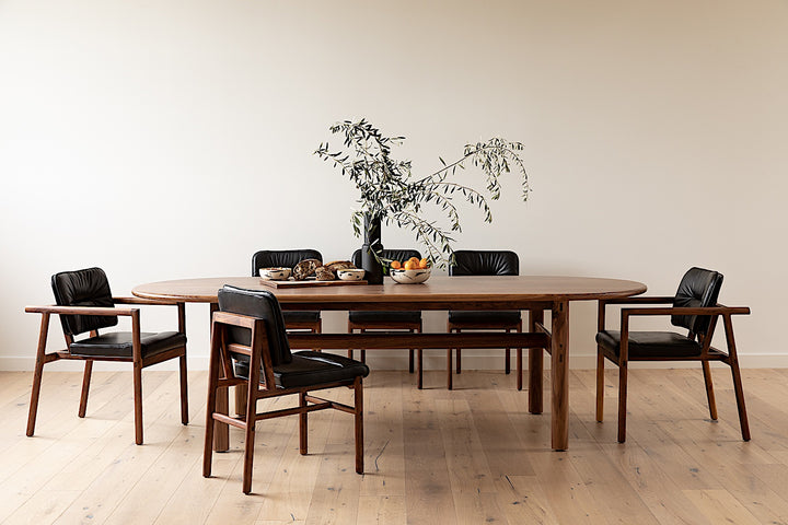 The PALANG Dining Table by Earl Home boasts a robust oval design in rich walnut, supported by four legs and a crossbeam. It comes on a plain white background and offers customizable lengths for perfect fitting in any space.