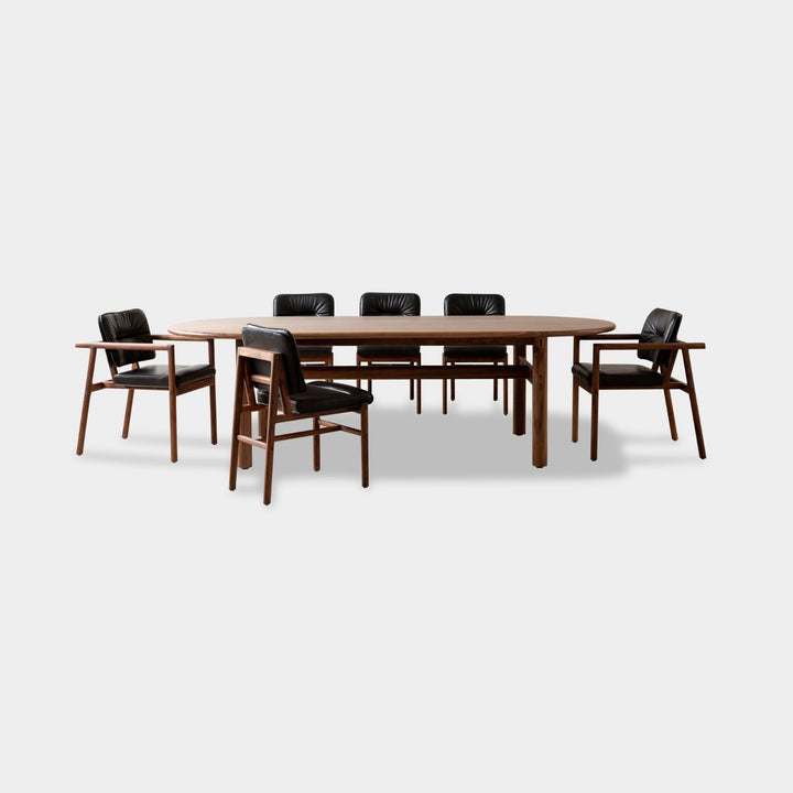 The PALANG Dining Table by Earl Home boasts a robust oval pill shape with bullnose edge design in rich walnut, supported by four legs and a crossbeam. It is available in white oak, maple, or ebonized oak.  This table comes in customizable lengths and top shapes including rectangular or live edge for perfect fitting in any space.